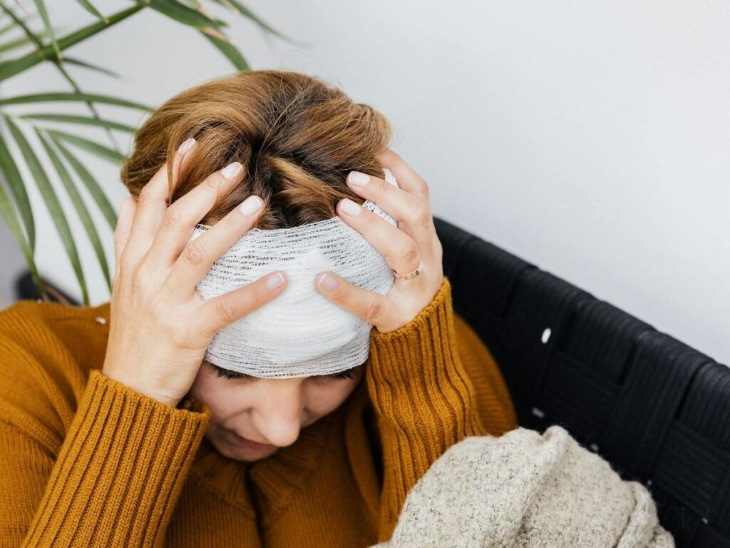 Senior woman with a head bandage holding her head in pain – head injury treatment and senior rehabilitation in Los Angeles.