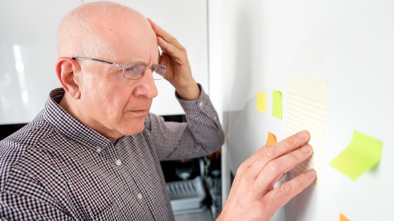 Senior man reviewing sticky notes on a whiteboard, symbolizing memory exercises and daily habits for healthy aging.