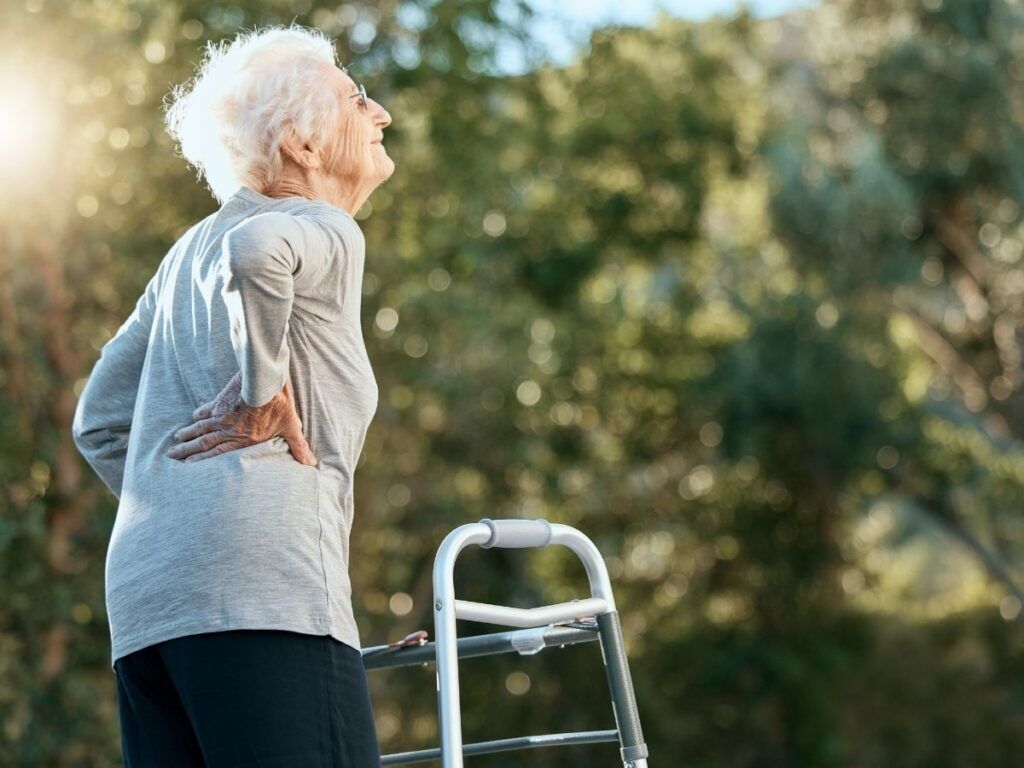 Senior woman holding her back while reviewing osteoporosis and compression fracture support.