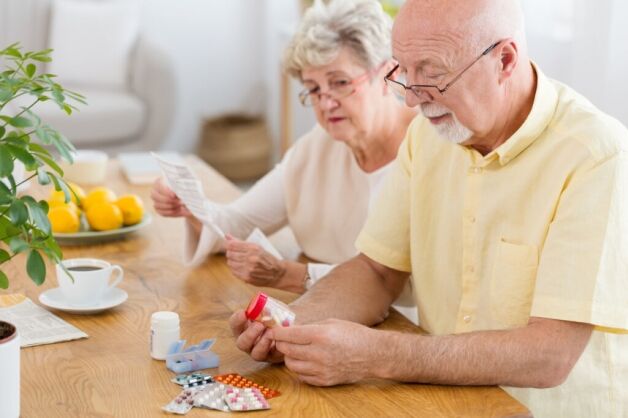 Senior couple reviewing prescription medications and pill containers at home, representing access to free medical supplies and senior healthcare support