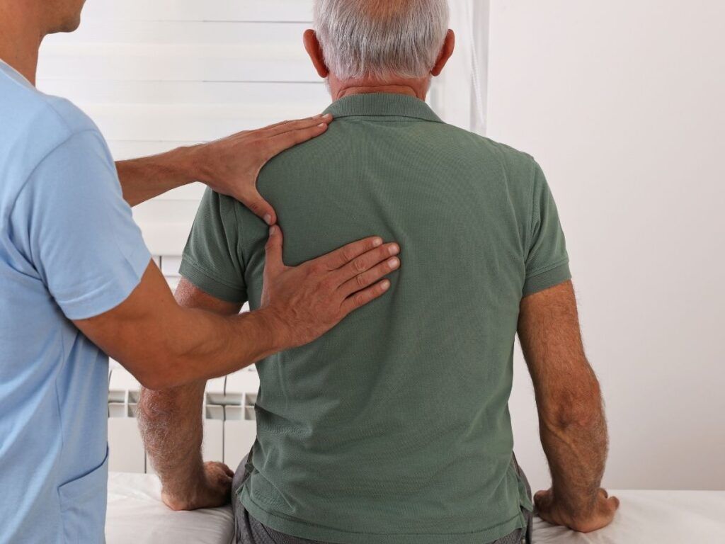 Senior man receiving support for lower back and sciatic nerve pain during a care visit.