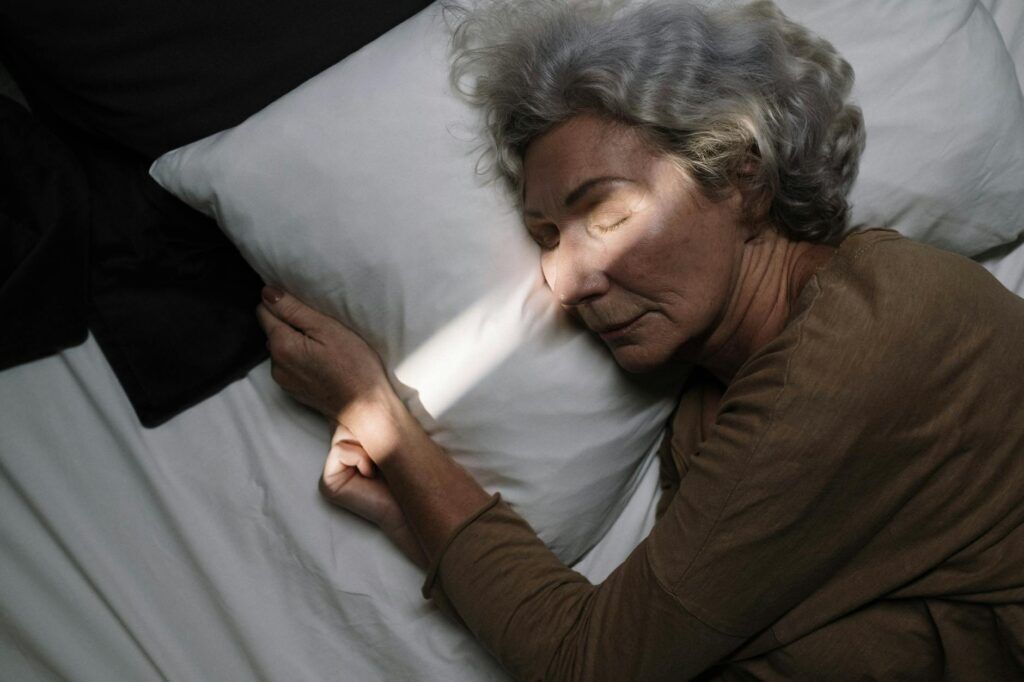 Un momento de serenidad: una anciana duerme plácidamente en una cama con iluminación tenue.