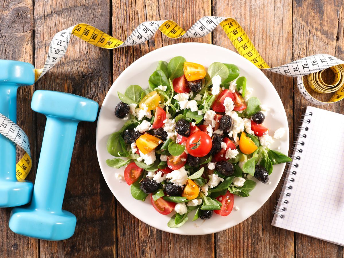 Colorful fresh salad bowl with dumbbells and tape measure – healthy habits for seniors supporting longevity, mental wellness & physical health.