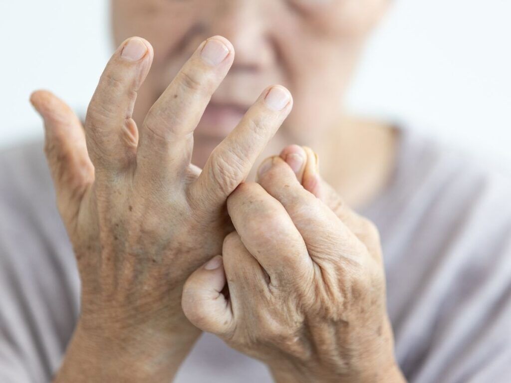 Senior woman holding painful hand joints while reviewing joint pain and arthritis support.